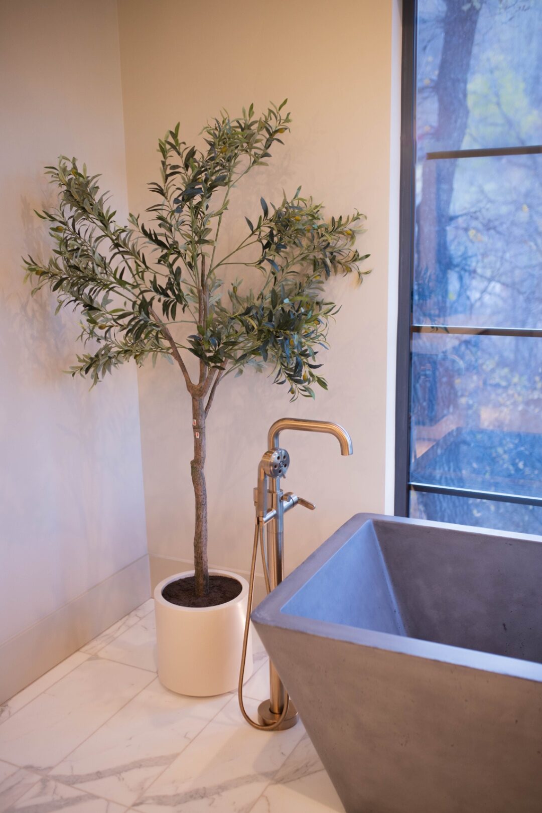 A pristine concrete vessel sink with brass fixtures and a styled olive tree beside it after a LivFlo bathroom service.