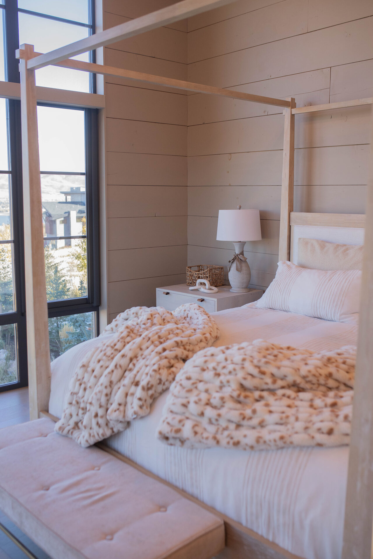 A freshly made canopy bed with chunky knit throws and crisp white pillows in warm afternoon light.