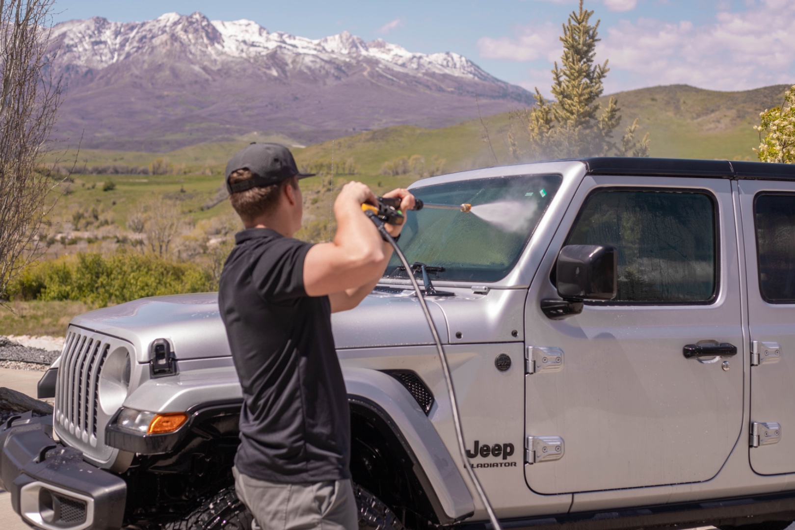 A LivFlo detailer rinses a Jeep with a pressure washer in front of the Wasatch range.