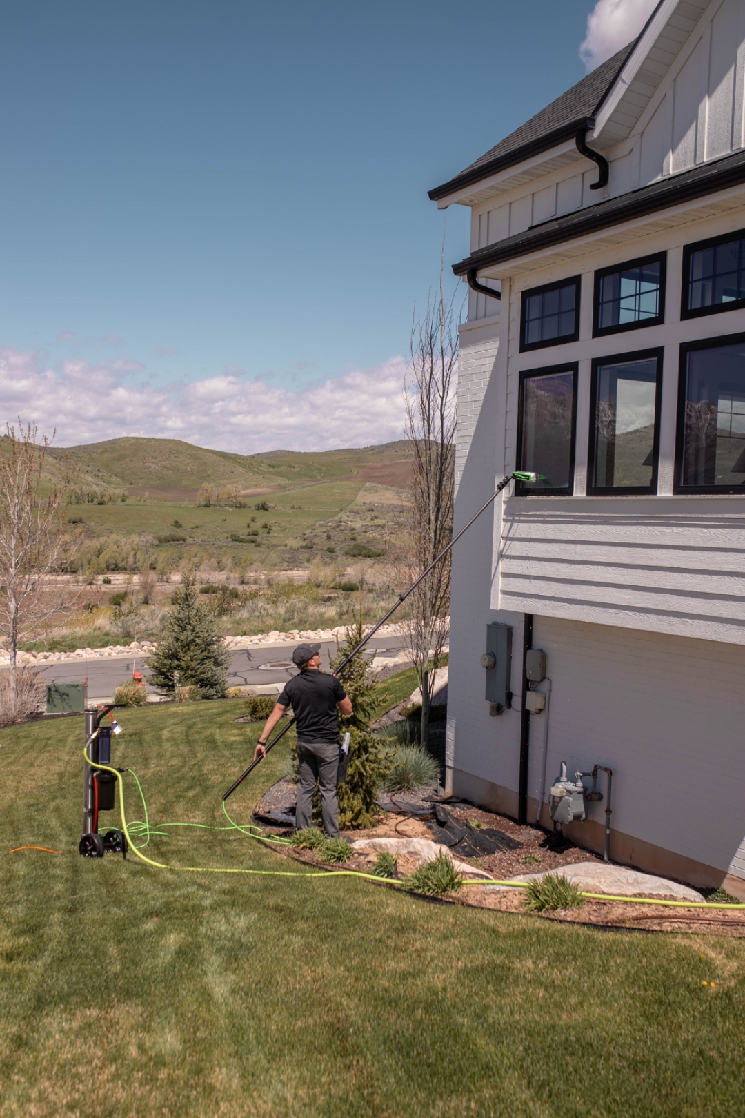 A LivFlo window cleaner working on a modern farmhouse with the Wasatch mountains in the background.