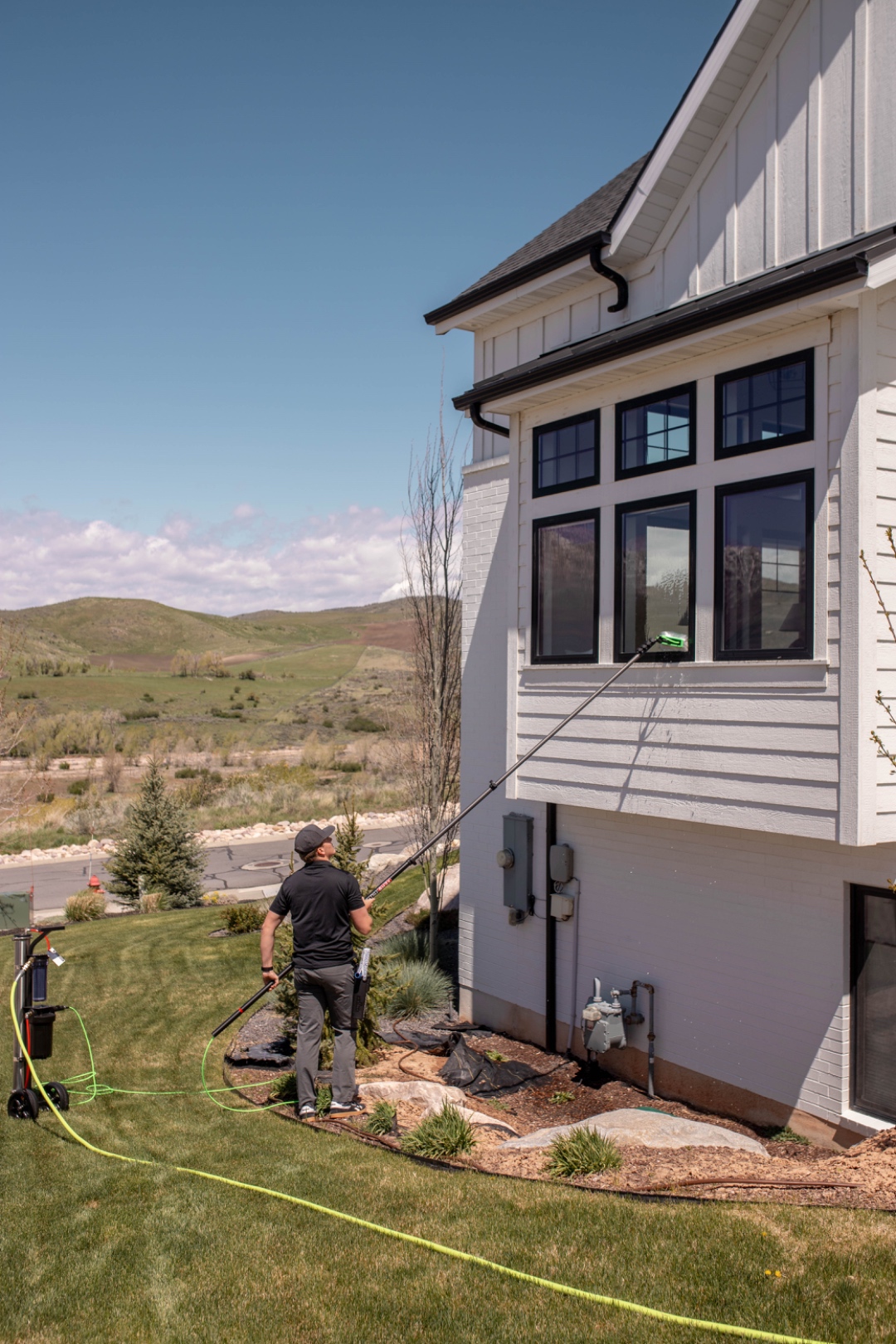 A LivFlo window cleaner using a water-fed pole on tall windows with Utah hills in the background.