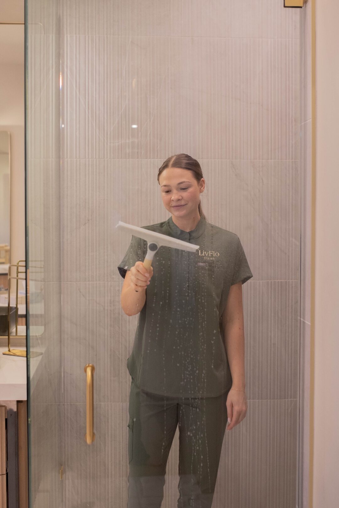 A LivFlo team member finishing a glass shower enclosure with a professional squeegee — perfectly streak-free.